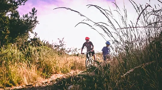A father and son riding bikes down an overgrown dirth path.